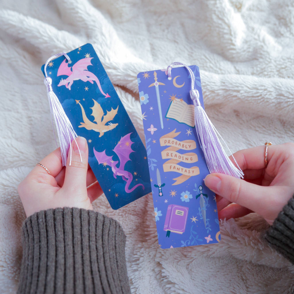 Two decorative bookmarks with tassels held by hands against a soft fabric background